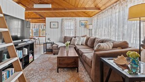 A cozy living room with a wooden ceiling, a brown sofa, a coffee table, and a TV. - Outdoor Cape Cod Oasis just 5 minutes to S Village Beach! (Dennis)