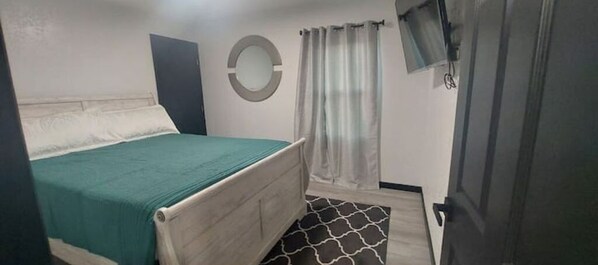 A bedroom with a bed, a round mirror, a curtain, and a television on the wall.