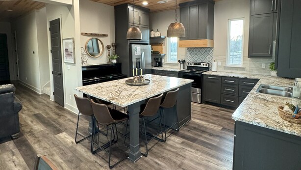 Una cocina moderna con una isla central, armarios oscuros y suelo de madera.