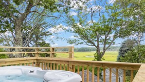 A hot tub on a wooden deck with a view of a grassy field and trees. - 7-bedroom home that sleeps 14.  5-minute walk to Moody Beach (Wells)