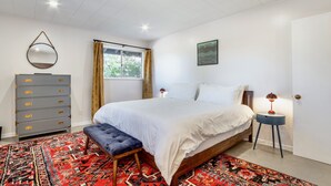 Une chambre à coucher avec un lit, une commode, un banc, un tapis et un tableau au mur.