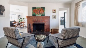 Un salon avec une cheminée en briques, des fauteuils à motifs et un coin repas comprenant une table et des chaises.