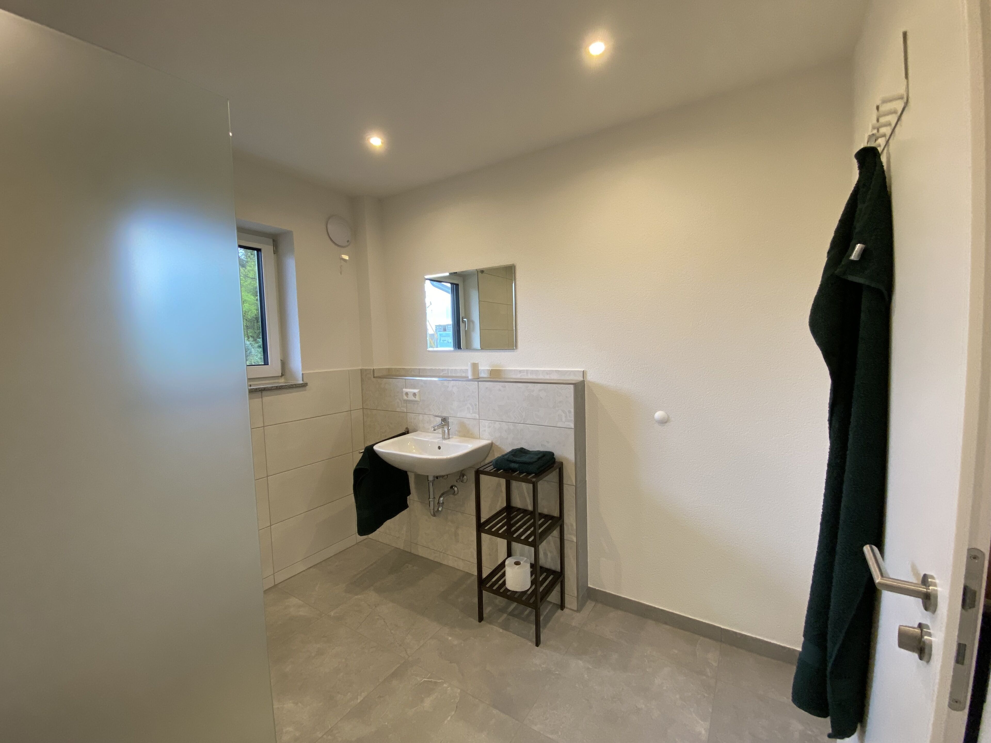 A bathroom with a white sink, a mirror, a towel rack, and a shelf with toiletries.