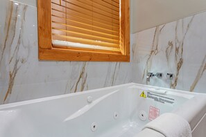 Une salle de bain moderne avec un mur en marbre, une fenêtre en bois et une baignoire ornée d’une étiquette d’avertissement.