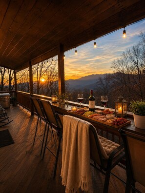 Eine Holterrasse mit Barbereich, Stühlen und Blick auf den Sonnenuntergang.