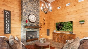 Acogedor interior de cabaña de troncos con chimenea, sofás de cuero, una mesa de centro de madera y un televisor.