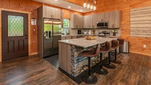Una cocina moderna con paredes de madera, una isla de granito y taburetes de bar.