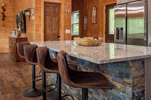 A kitchen with a granite countertop, wooden bar stools, a woven basket, and a stainless steel refrigerator. - Brand New Luxury 3/3.5 Cabin Great Mountain Views, Hot Tub, Ober Gatlinburg Ski  (Gatlinburg)