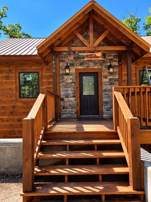 A wooden cabin with a stone facade, a black front door, and a sign that reads 'Welcome to Daisy's Cabin.'