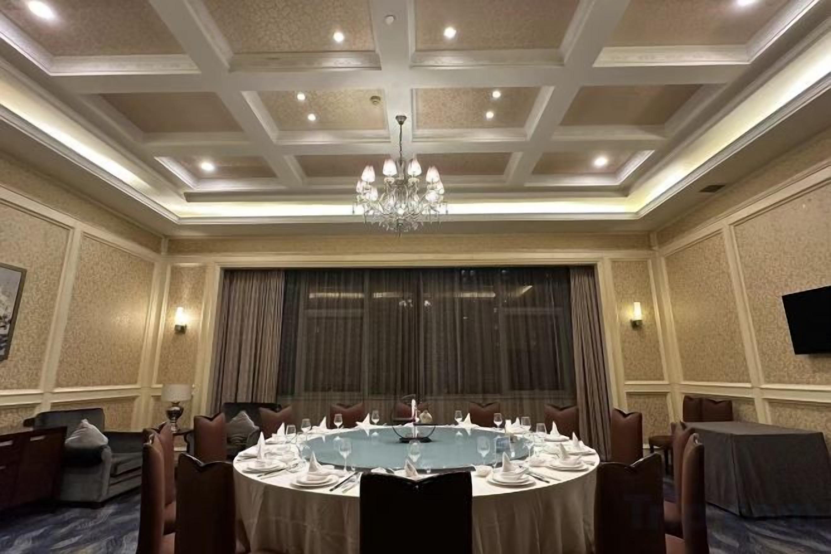 Una sala de conferencias con una mesa redonda, sillas, una araña y una televisión en la pared.