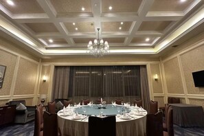 Une salle de conférence avec une table ronde, des chaises, un lustre et un téléviseur fixé au mur.