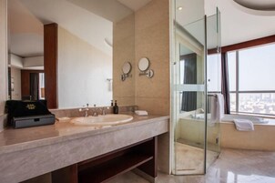 Un baño moderno con un espejo grande, dos lavamanos, ducha con cerramiento de vidrio y vistas a la ciudad.