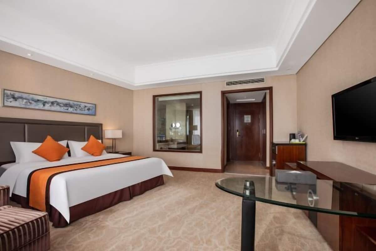 Quarto de hotel com cama grande, escrivaninha, televisão e espelho.