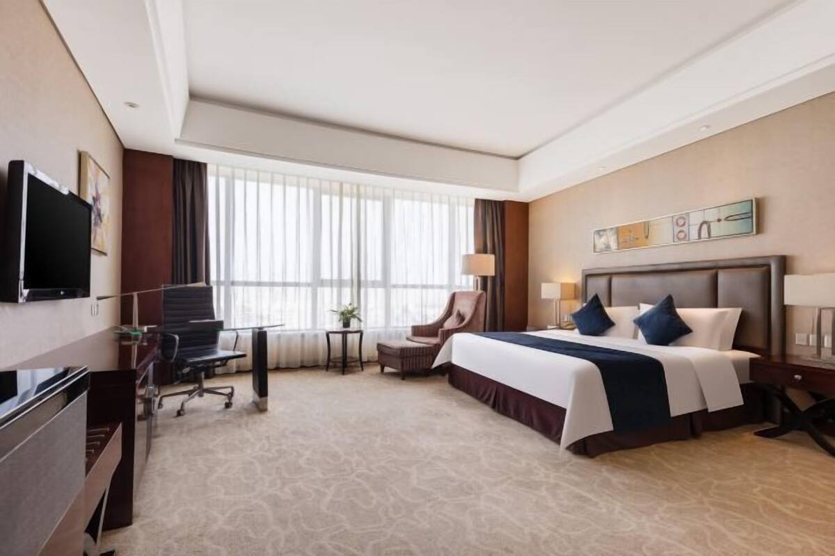 Quarto de hotel com uma cama grande, uma escrivaninha, uma cadeira e uma televisão.