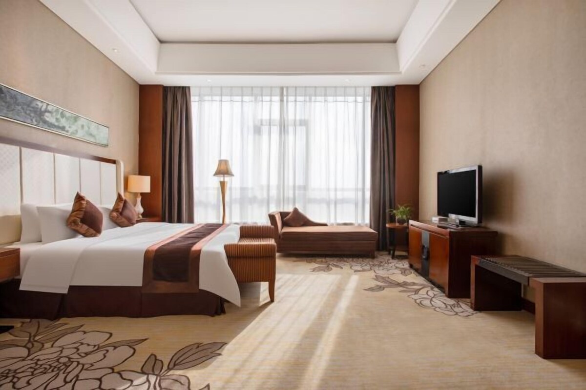 A hotel room with a large bed, a sofa, a TV, and a desk.