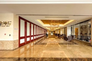 Un pasillo de hotel con piso de mármol pulido, una zona de recepción con candelabro y un cartel con el nombre del hotel.