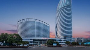 Un hotel moderno con fachada curva, una entrada destacada y un edificio cilíndrico alto contiguo.