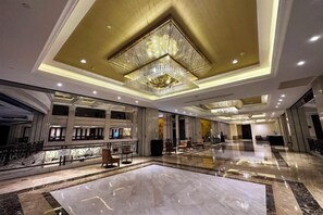 Un hall d’entrée spacieux, agrémenté d’un grand lustre, d’un sol en marbre et de plusieurs espaces aménagés pour s’asseoir.