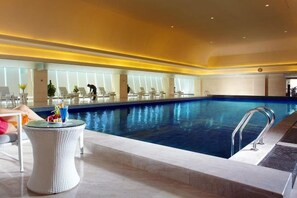 Una piscina interior con zona de descanso, sillas y una mesa con bebidas.