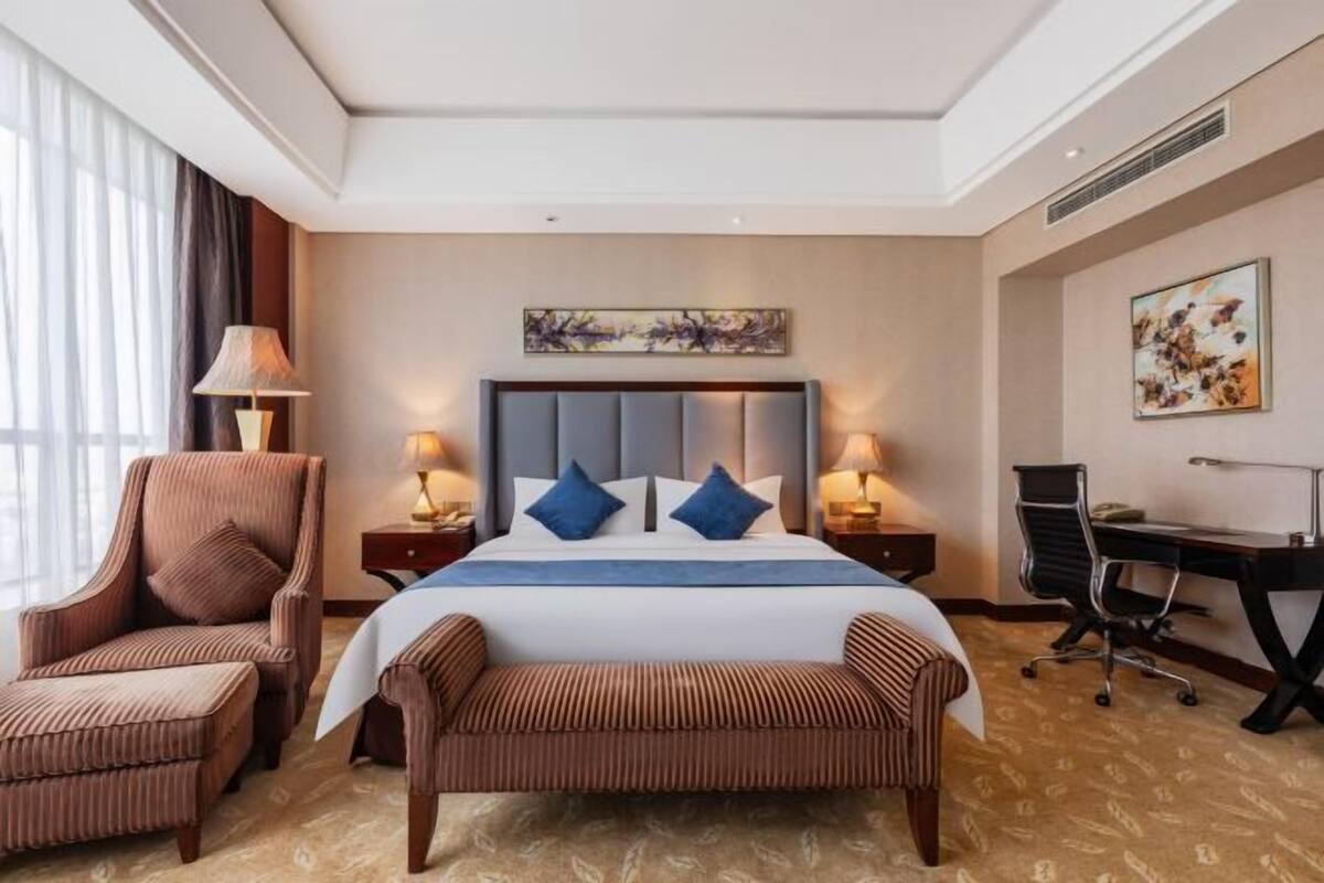 Quarto de hotel com cama, escrivaninha, cadeira e um banco.