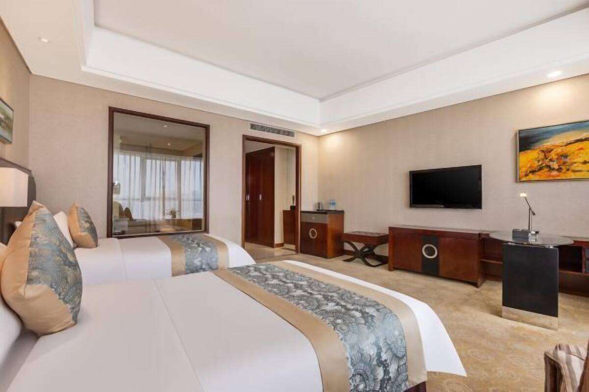 Quarto de hotel com uma cama grande, televisão, escrivaninha e espelho.
