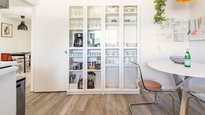 A modern kitchen with white cabinetry, a dining area with a round table and metal chairs, and a coffee machine.