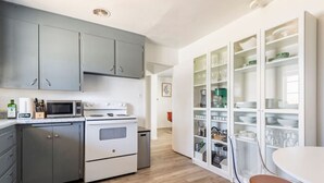 A kitchen with grey cabinets, a white stove, and a glass-fronted pantry.
