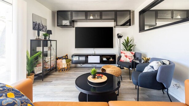 A modern living room with a flat-screen TV, comfortable seating, a coffee table, and a bookshelf.