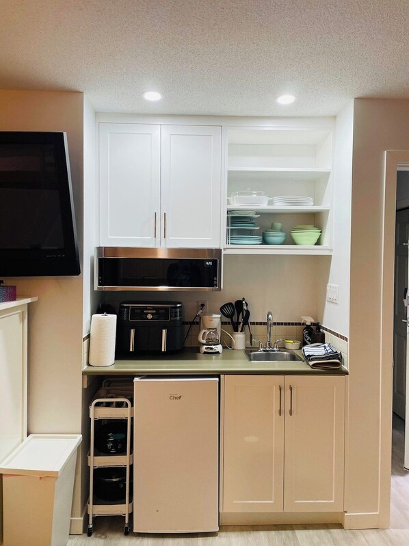A compact kitchenette with white cabinets, a microwave, a coffee maker, and a small refrigerator.