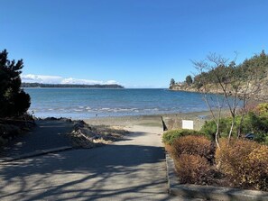 A coastal pathway leading to a beach with a clear view of the sea and distant mountains.