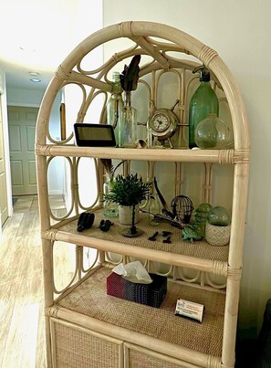 A wicker shelf with various decorative items including a clock, bottles, and a small plant.