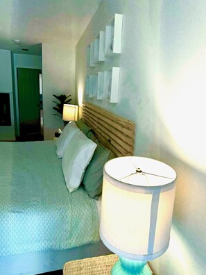 A hotel room with a bed, a lamp, a wall-mounted shelf, and a door leading to another room.