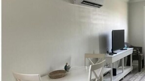 A room with a white dining table, two white chairs, a small woven basket, a flat-screen TV on a white stand, and an air conditioning unit mounted on the wall. - Aqua Diver is a darling 1 BR house on the East end of Panama City Beach, Florida (Panama City)