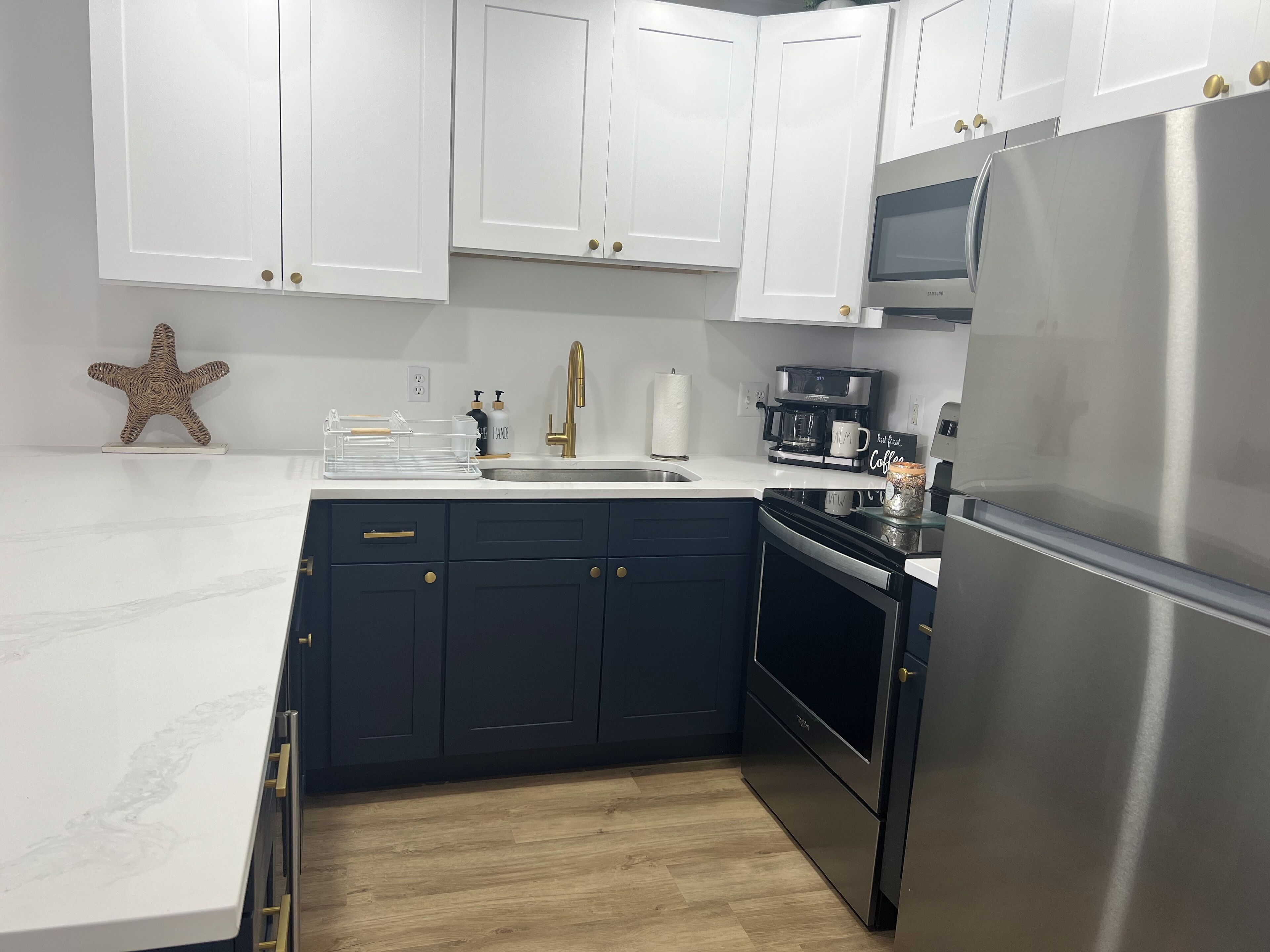 Una cocina moderna con armarios blancos, un refrigerador de acero inoxidable, una cafetera y piso de madera.