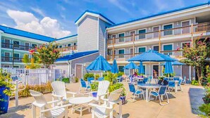 A hotel patio with outdoor seating and umbrellas, surrounded by a multi-story building with balconies. - Completely Renovated Perfect Beachtown Escape for the Whole Family (Ocean City)