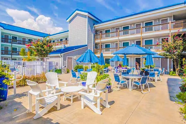 A hotel patio with outdoor seating and umbrellas, surrounded by a multi-story building with balconies.