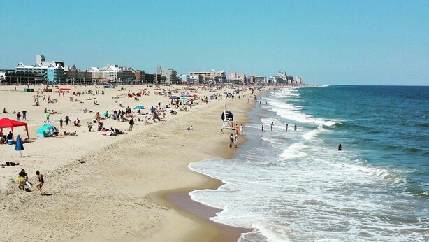 A wide beach with people and umbrellas, a lifeguard tower, and buildings in the background. - Completely Renovated Perfect Beachtown Escape for the Whole Family (Ocean City)