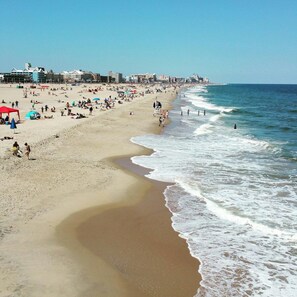 A wide beach with people and umbrellas, a lifeguard tower, and buildings in the background.