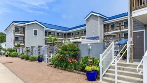 A multi-story hotel with a brick pathway leading to the entrance, stone pillars, and a blue awning over the stairs. - Completely Renovated Perfect Beachtown Escape for the Whole Family (Ocean City)
