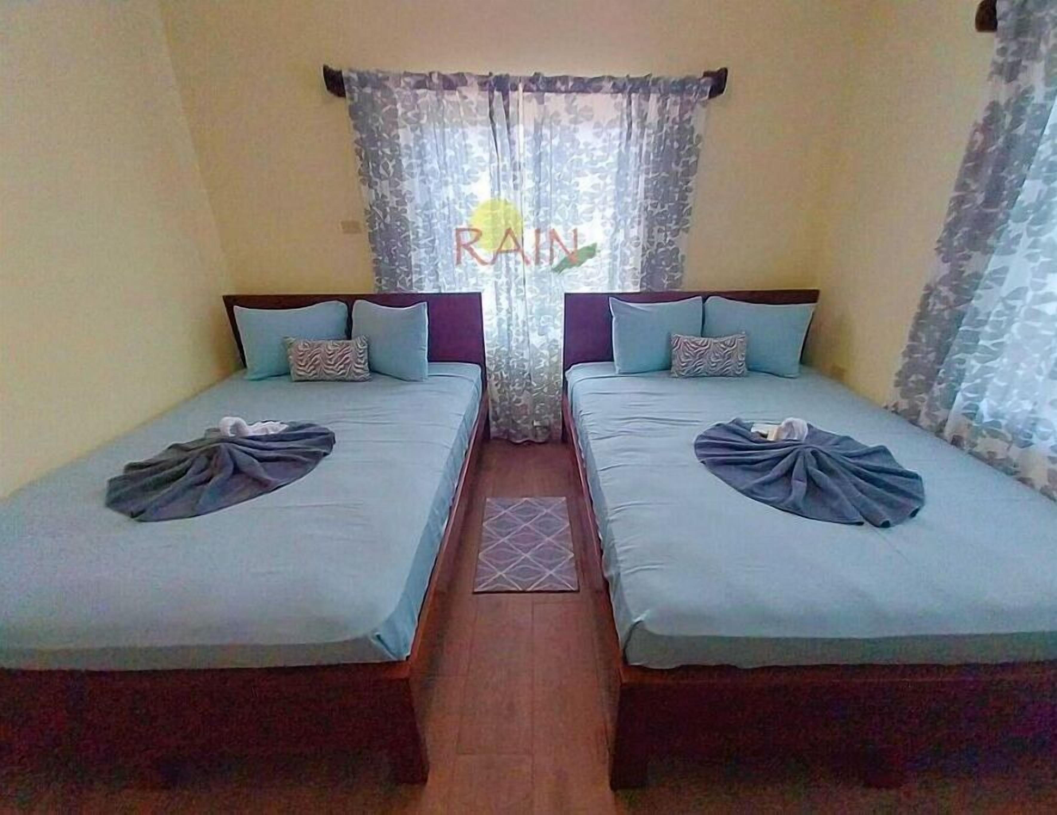 A room with two single beds, each with a pillow and a blanket.