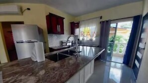 Une cuisine moderne dotée d’un plan de travail en marbre, d’appareils électroménagers en acier inoxydable et d’une porte-fenêtre coulissante donnant sur un balcon.
