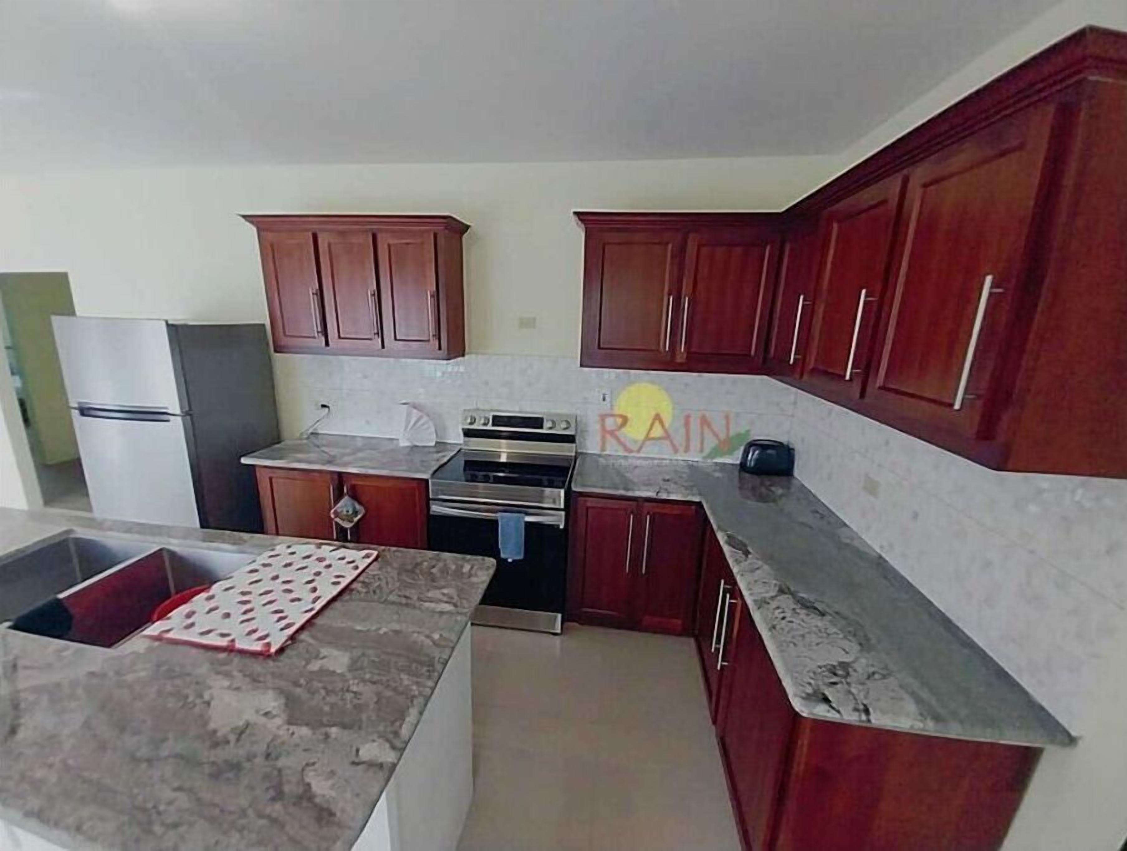 A kitchen with wooden cabinets, a stainless steel refrigerator, an oven, and a marble countertop.