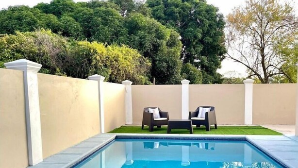 Une piscine rectangulaire, agrémentée de deux chaises longues et d’une petite table, le tout entouré d’un mur de couleur beige et d’une végétation luxuriante.