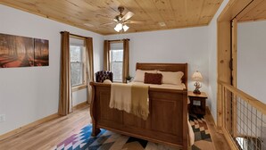 Une chambre avec un plafond en bois, un lit avec une tête de lit, une table de chevet, une lampe et une fenêtre avec des rideaux.
