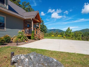 A two-story house with a stone fireplace, a covered porch, and a large rock in the foreground. - Blue Sky Cabin in Jefferson NC - Hot Tub, Firepit, Axe throwing, and more! (Jefferson)