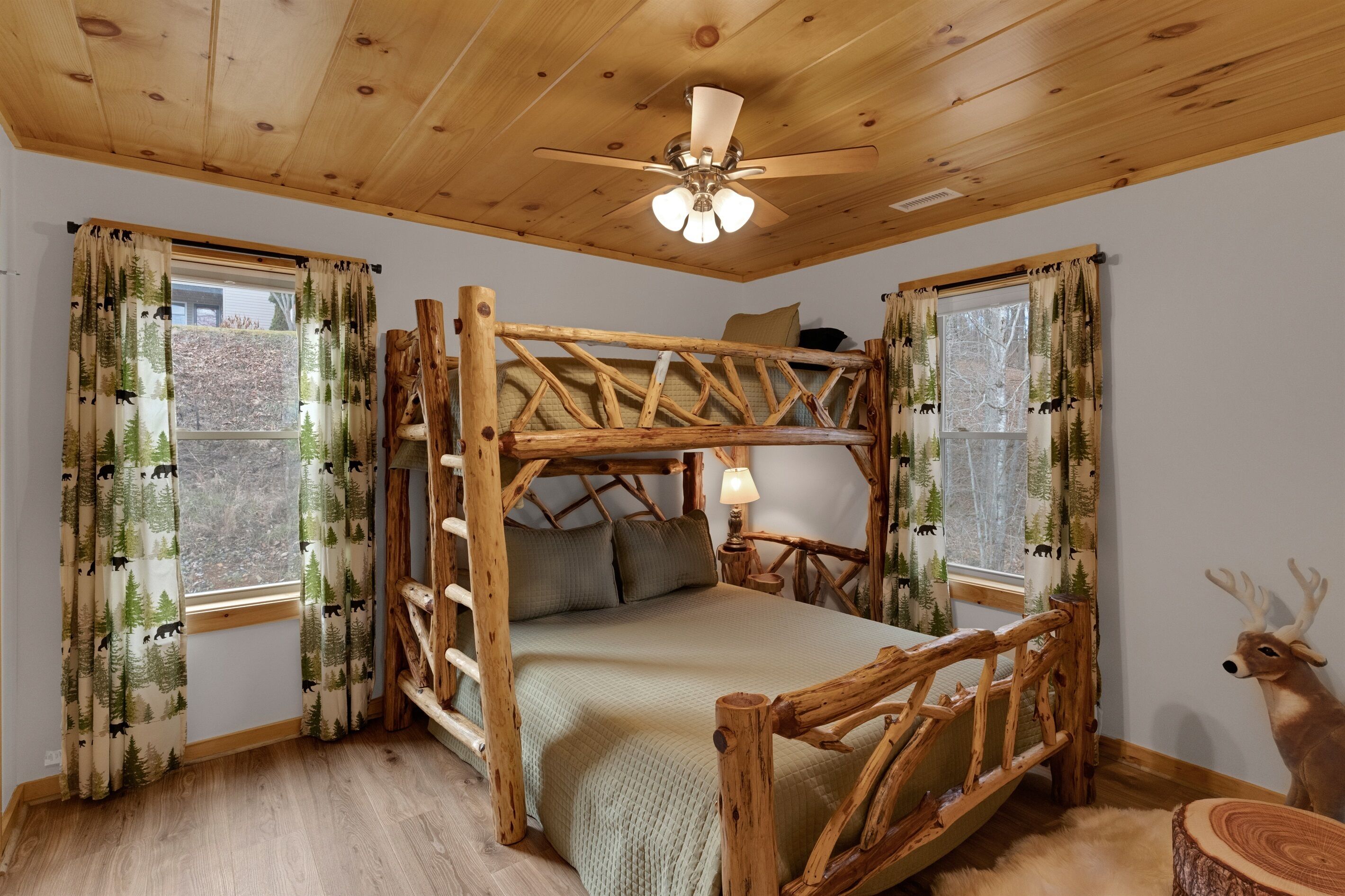 Un dormitorio rústico con una cama litera de madera, ventilador de techo y cortinas con motivos forestales.