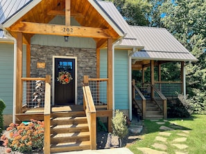 Un chalet doté d’une façade en pierre, d’un porche en bois et d’un escalier menant à une zone abritée.