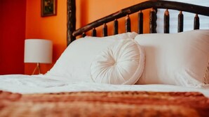 Un letto con lenzuola bianche e testiera in legno, una lampada da comodino e una parete rossa.