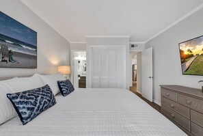 A bedroom with a large bed, a dresser, and a TV on the wall.