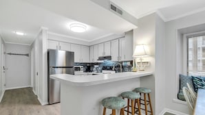 Cocina moderna con armarios blancos, electrodomésticos de acero inoxidable, una isla central con taburetes y una ventana con persianas.